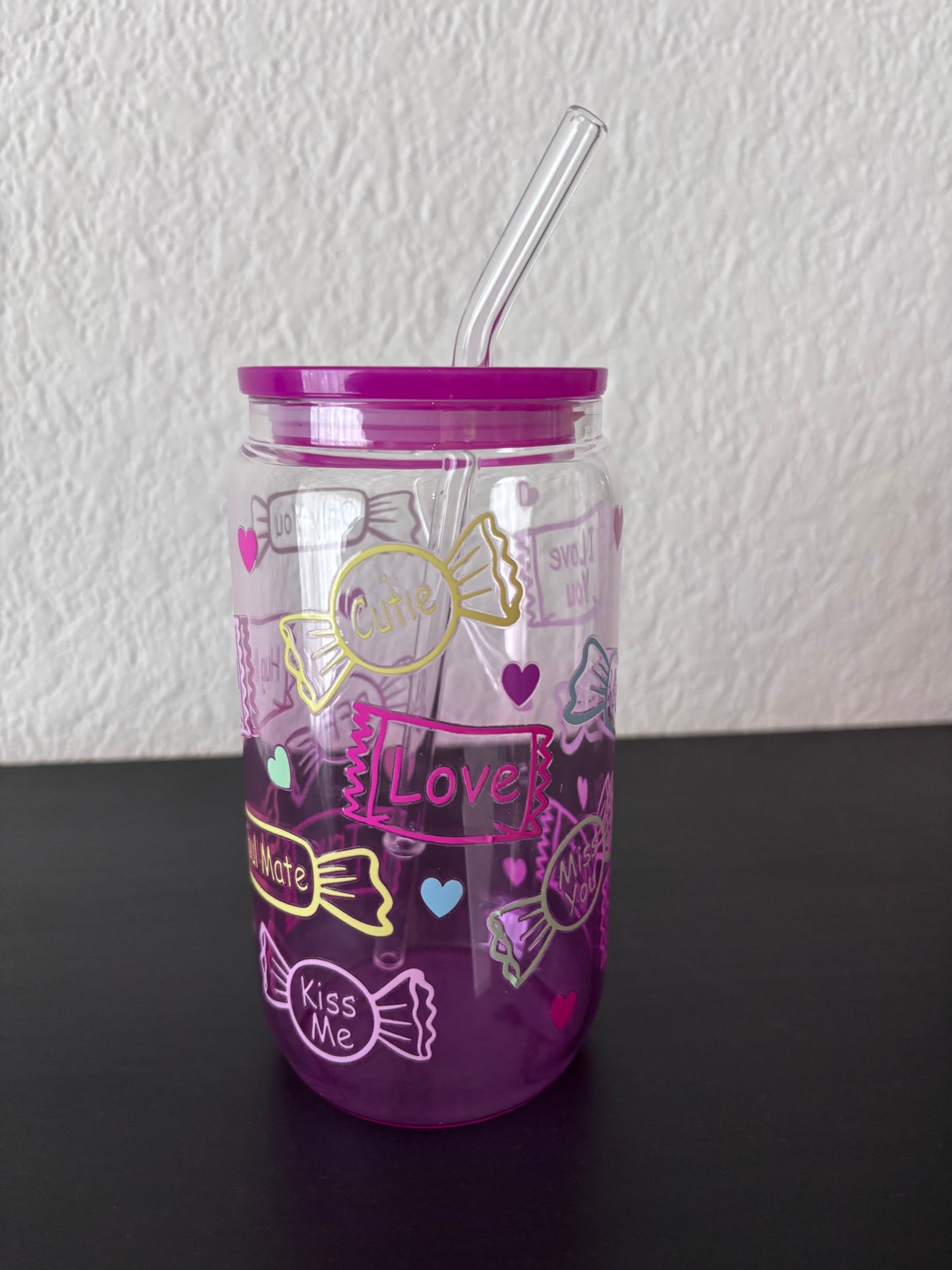 Paarse drinkbeker met transparant rietje, versierd met snoepjes en teksten als “Cutie”, “Love” en “Kiss Me”,