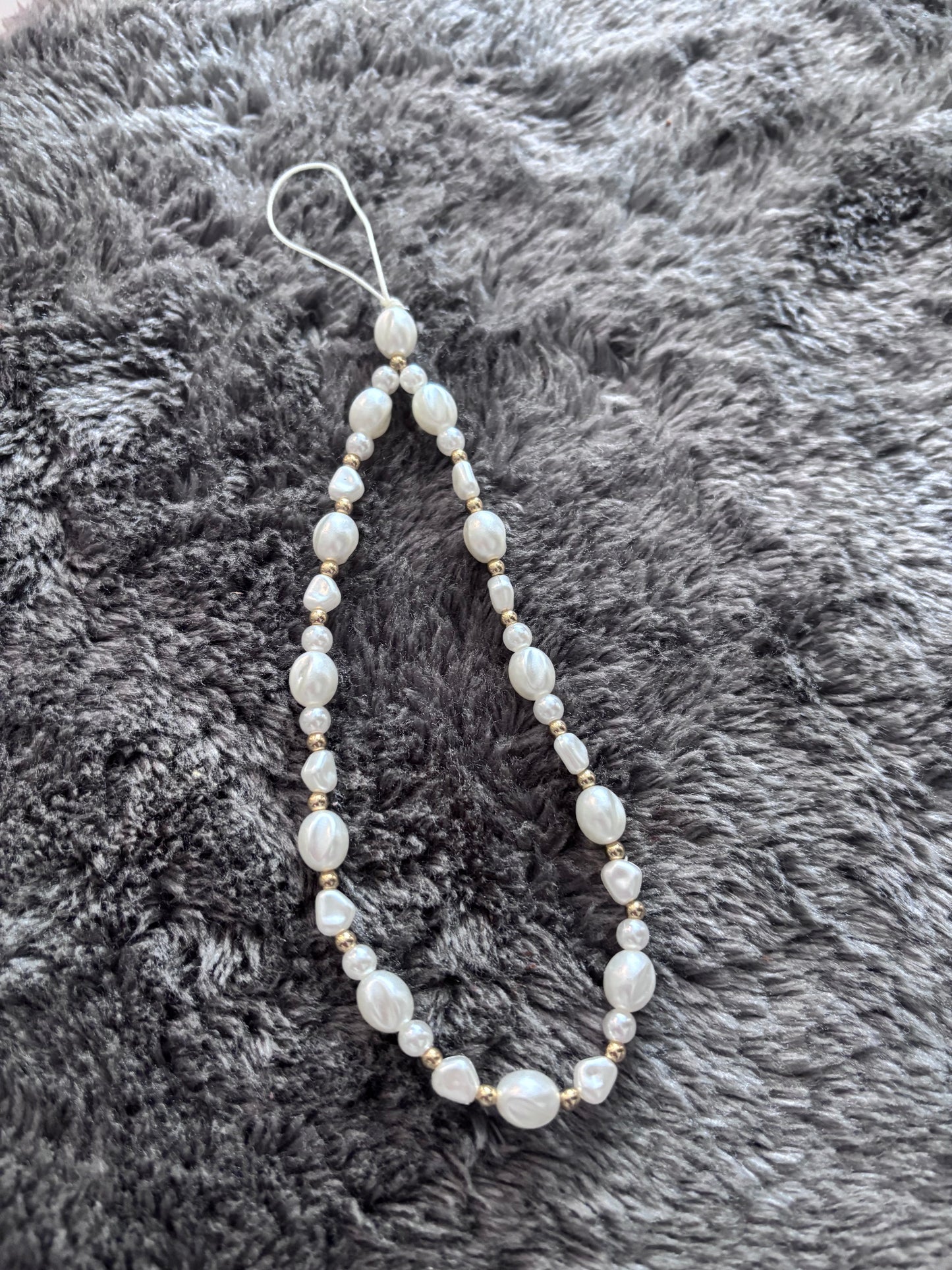 Handgemaakt telefoonkoord met witte parelkralen en goudkleurige details op een grijze zachte achtergron