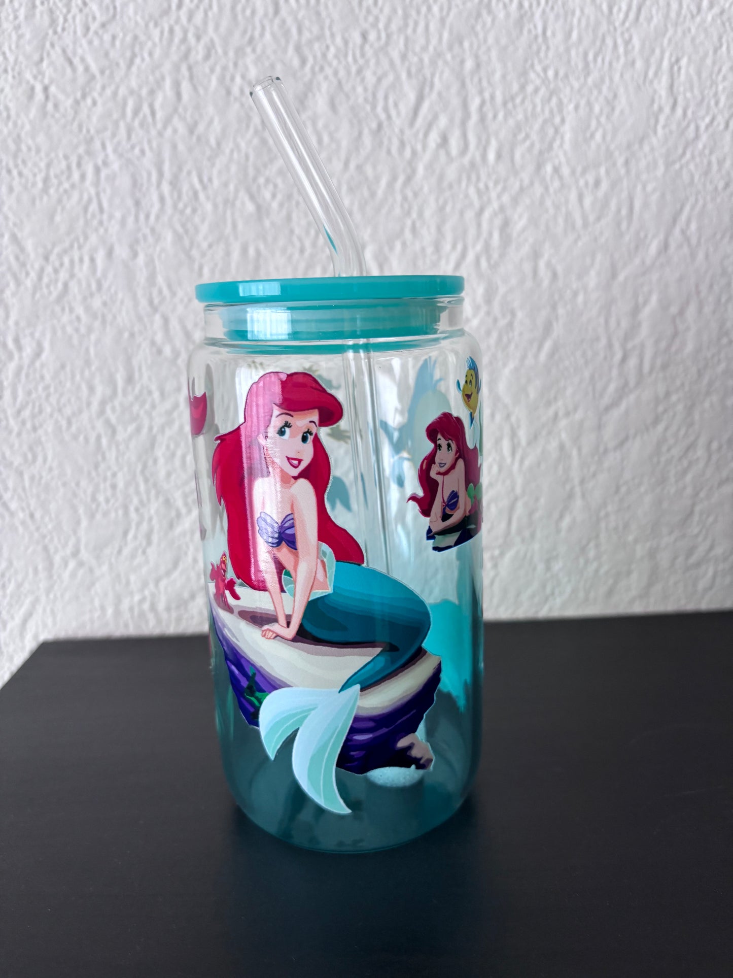 1️⃣ Herbruikbare drinkbeker met turquoise deksel, transparant rietje en kleurrijke zeemeerminprint op een zwarte ondergrond.