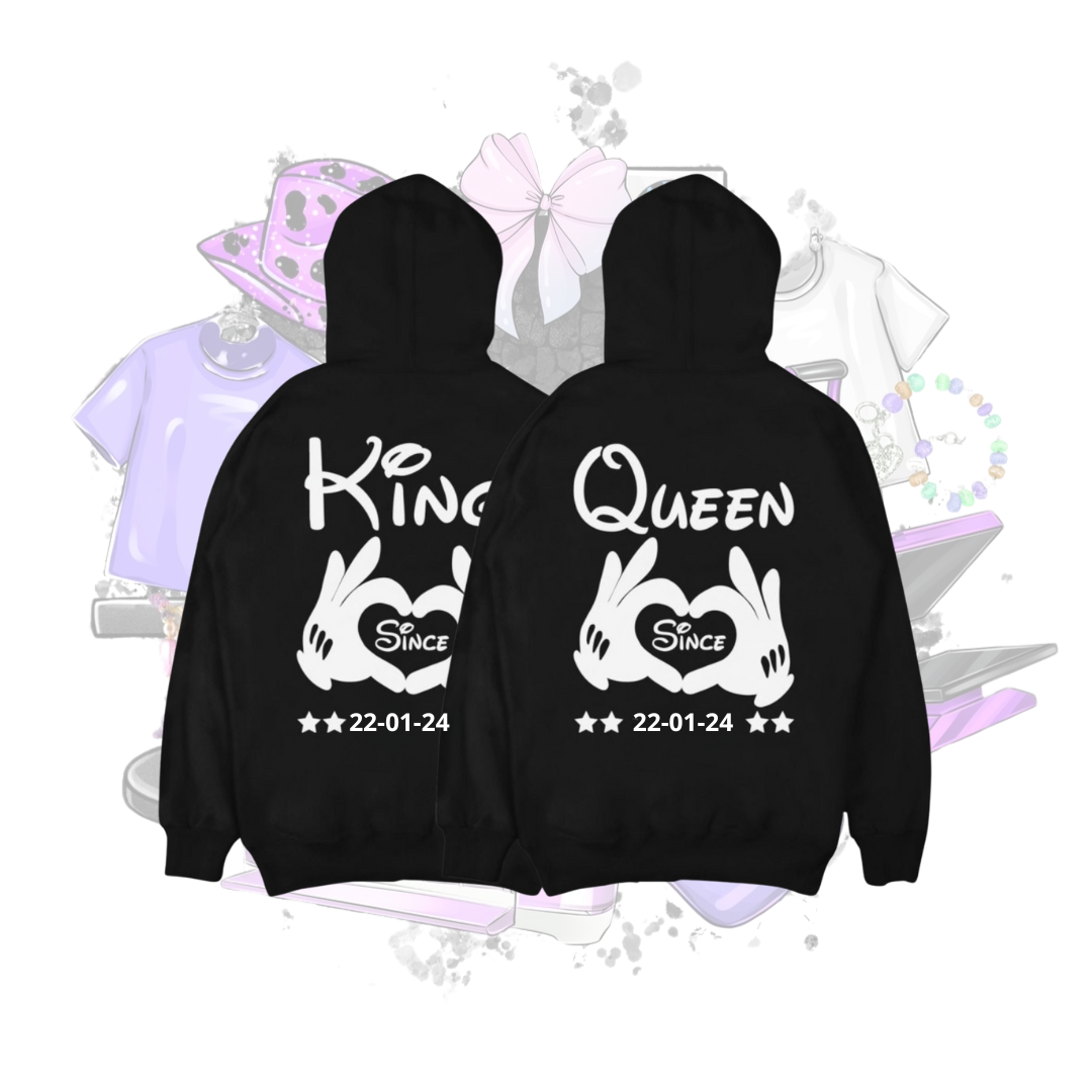Een set van twee zwarte hoodies met witte opdruk. De linker hoodie heeft het woord King en de rechter Queen, beide met een hart en handen die een hartvorm maken samen met de datum die voor jou passend is. Ideaal voor koppels als gepersonaliseerd cadeau