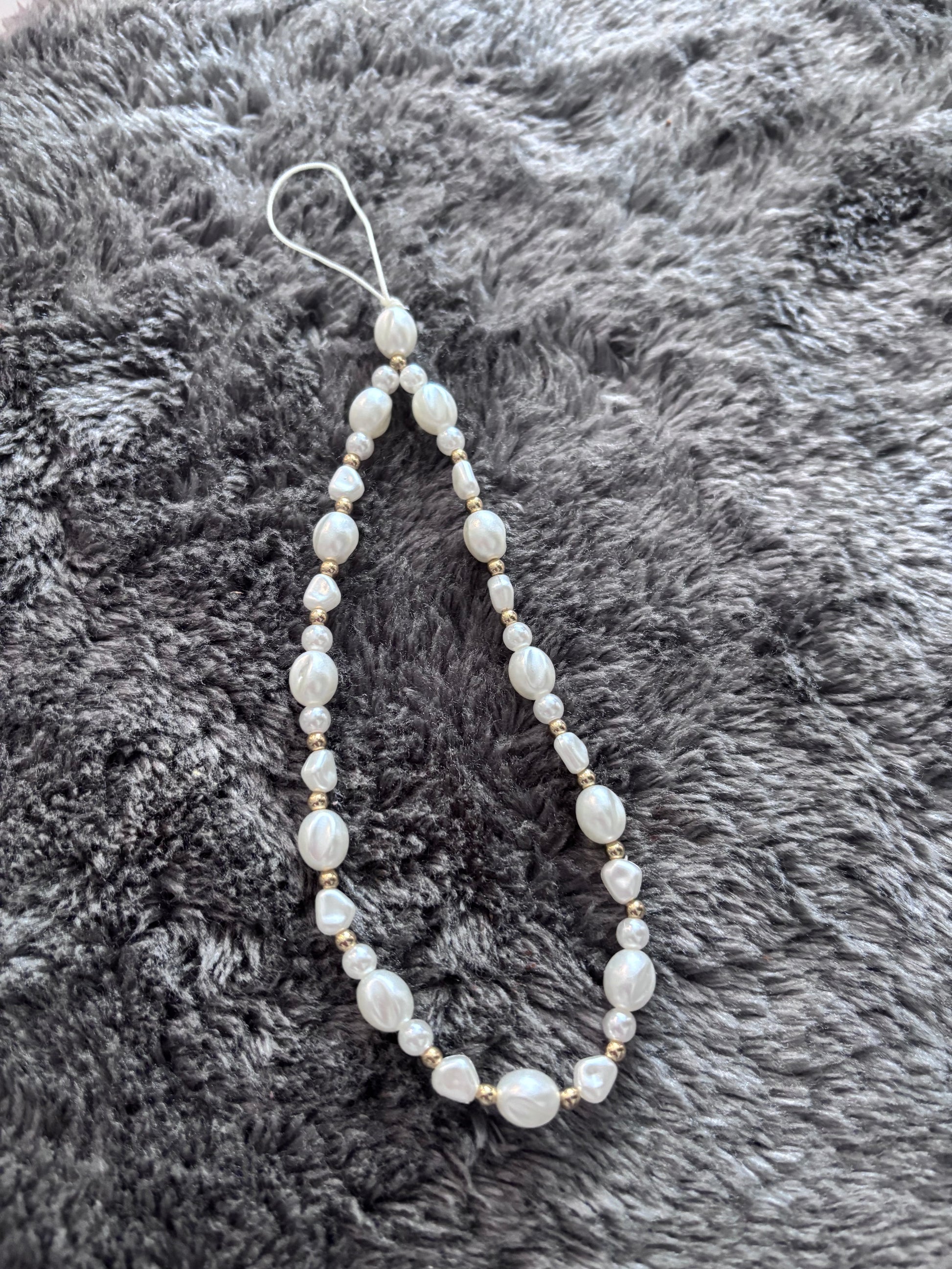 Handgemaakt telefoonkoord met witte parelkralen en goudkleurige details op een grijze zachte achtergron